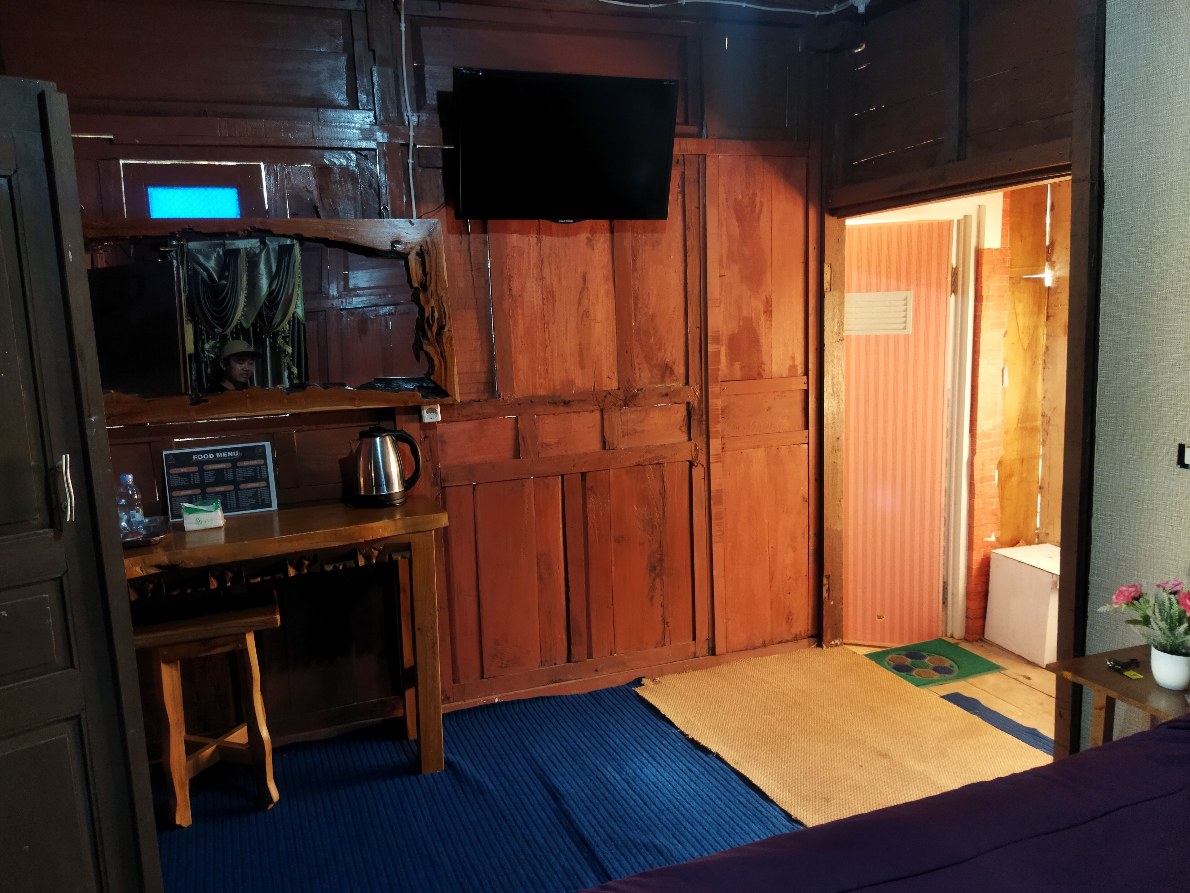 Une pièce de taille modeste, avec un bureau en bois, un téléviseur fixé au mur et un petit tabouret.