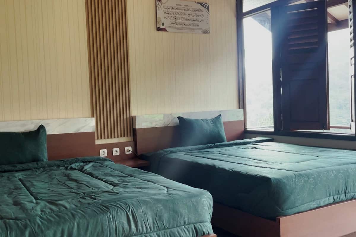 Two single beds with green bedding in a room with wooden paneling and a window with a view.