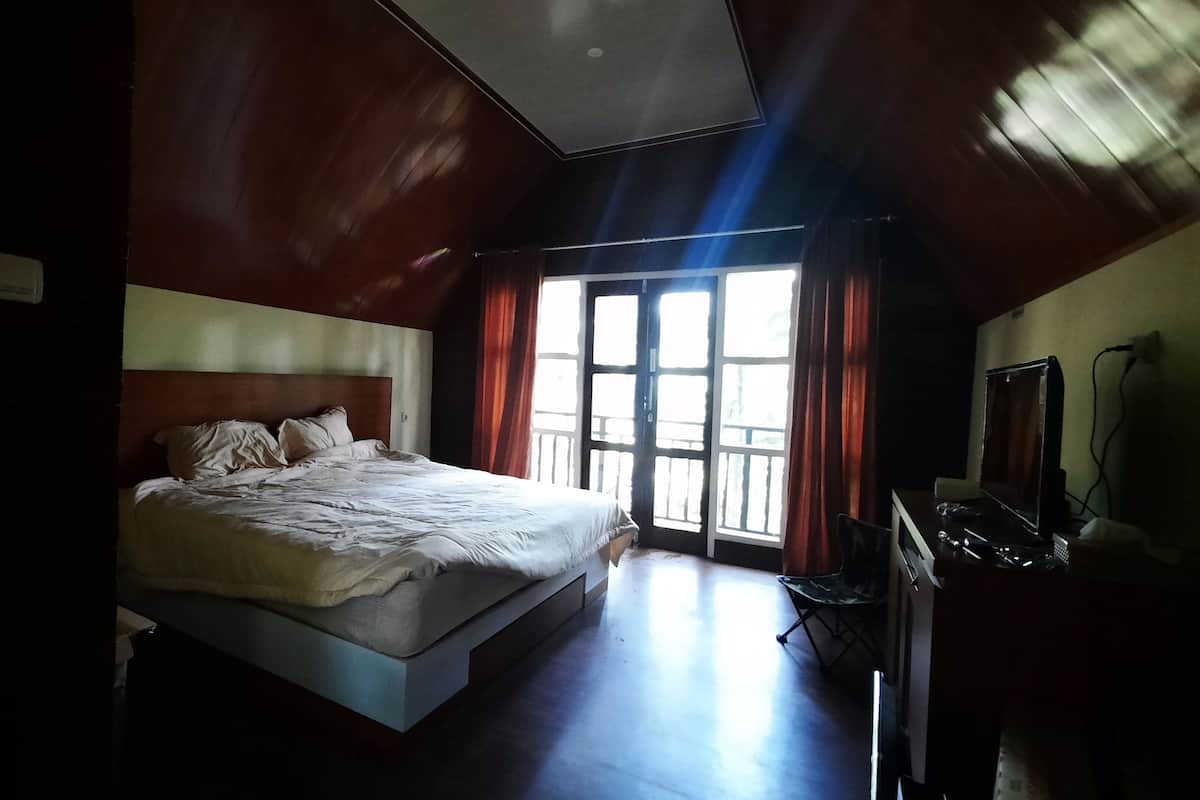 A bedroom with a large bed, a desk with a computer, and a window with curtains.