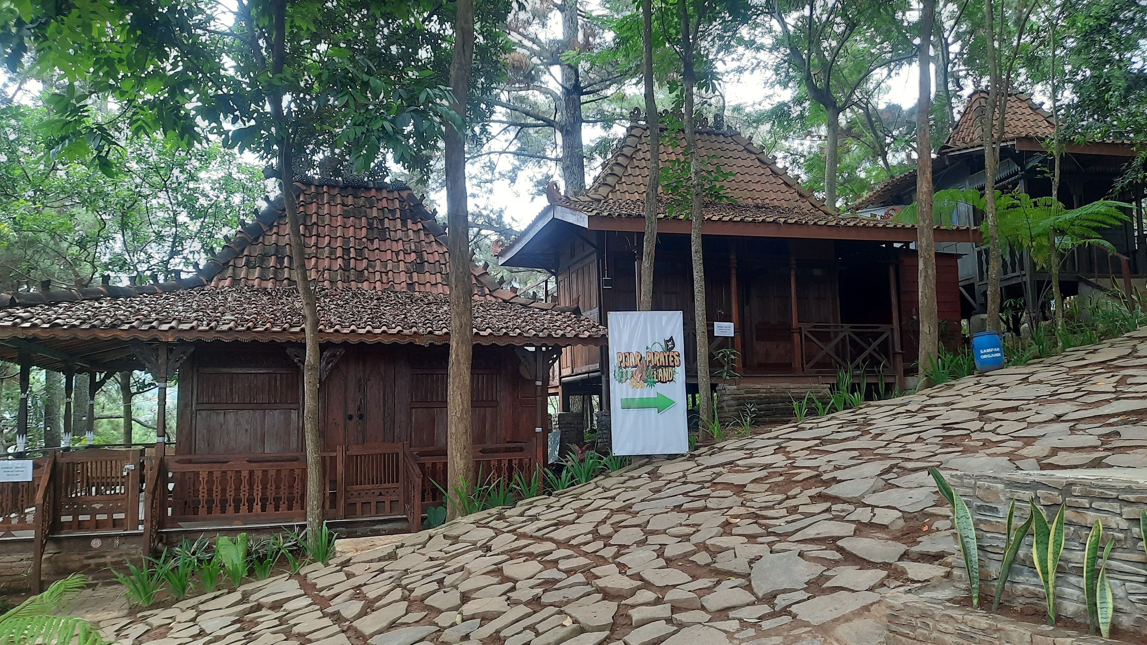 A rustic wooden building with a tiled roof, surrounded by lush greenery and stone pathways.