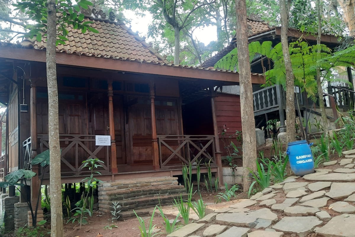 A wooden cabin with a tiled roof, surrounded by trees and greenery.