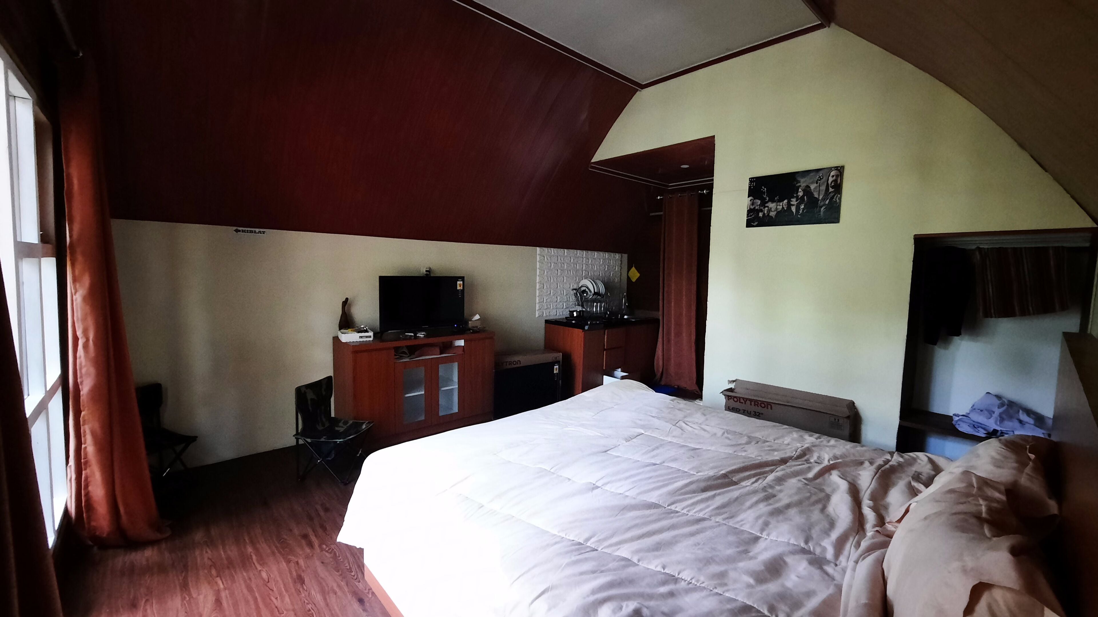A bedroom with a large bed, a television on a wooden cabinet, and a small desk.
