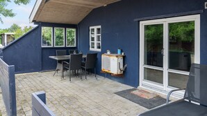 Un patio cubierto con una mesa, sillas, una kitchenette pequeña y un ventanal corredera.