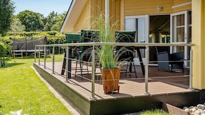 A yellow building with a covered outdoor area featuring a wooden deck, metal railing, and outdoor furniture.