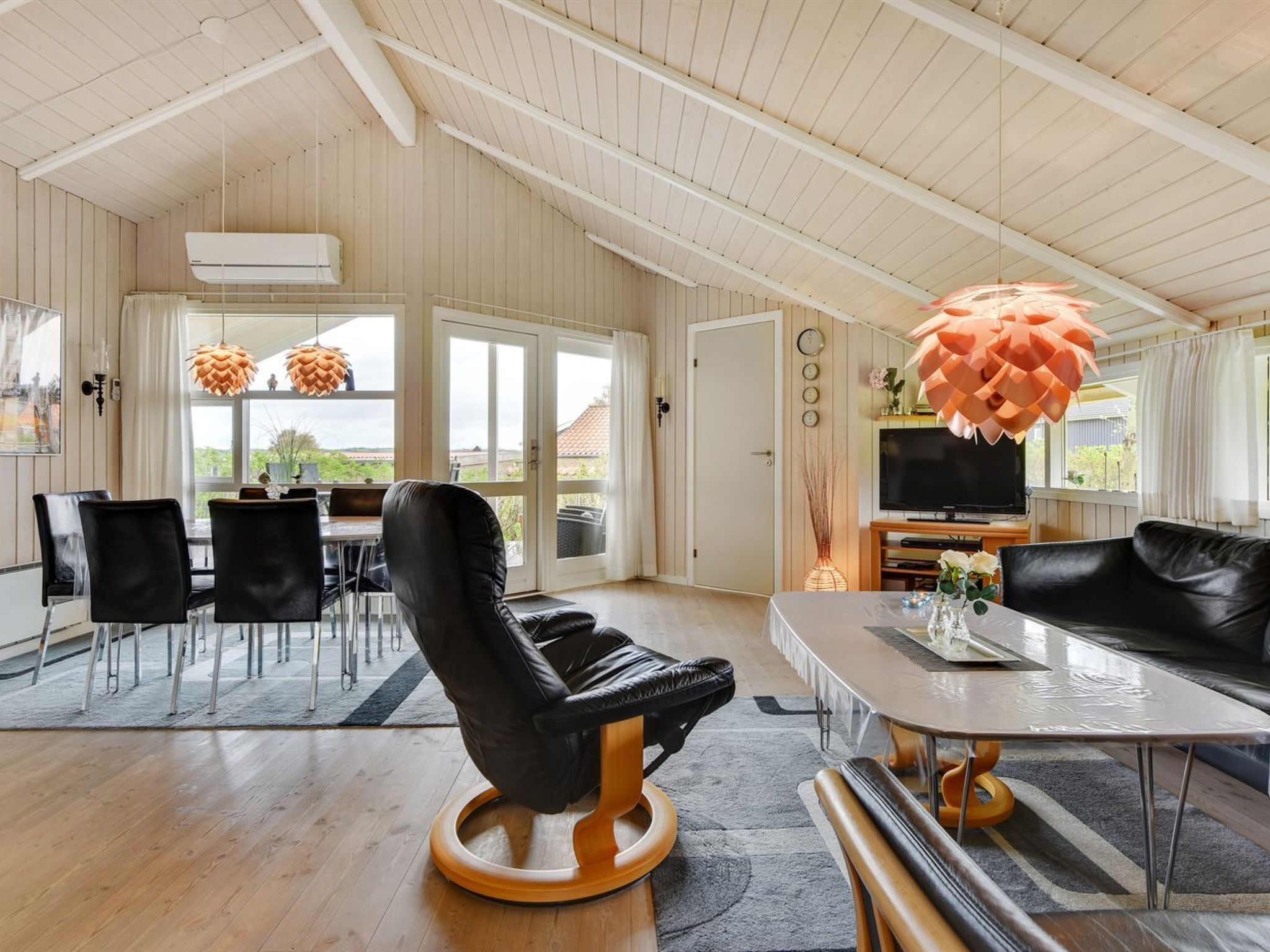 A spacious living area with a black leather sofa, a wooden coffee table, and a dining area with a table and chairs.