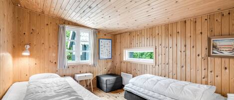 Une pièce aux murs lambrissés, comprenant deux lits, une petite table, une chaise et une fenêtre.
