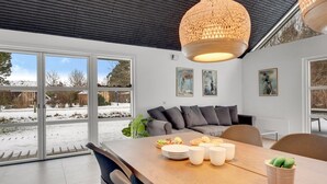 Ein moderner Essbereich mit Holztisch, grau bezogener Couch und einer großen, gewebten Pendelleuchte.