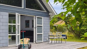 Ein Haus mit einer Holzterrasse, einer Schiebetür und einem kleinen Garten mit Gartenmöbeln.