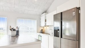 Een moderne keuken met een roestvrijstalen koelkast, witte kasten en een groot raam met zonwering.