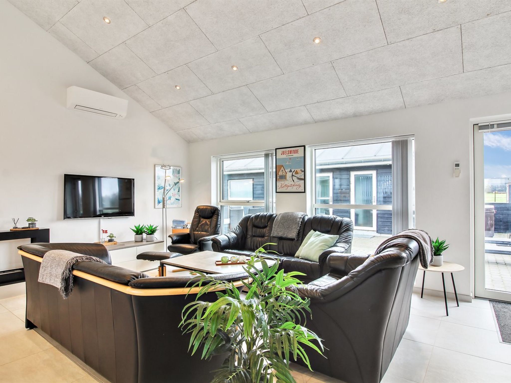 Una sala de estar moderna con un amplio sofá en forma de L, un televisor de pantalla plana y un ventanal con vistas al exterior.