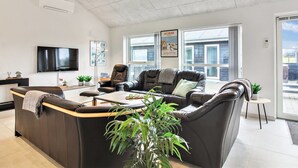 Een moderne woonkamer met een grote hoekbank, een flatscreen televisie en een groot raam met uitzicht op buiten.