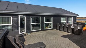 Een modern huis met een patio, inclusief een tafel en stoelen, een overdekte zithoek en grote ramen.