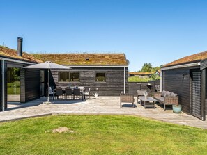 Et moderne hus med en terrasse, havemøbler og en velplejet græsplæne.