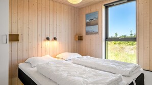Un dormitorio con una cama, paredes de madera, un ventanal y vistas al exterior.