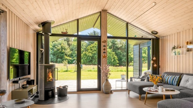 Una sala de estar moderna con chimenea, un sofá, un televisor y un amplio ventanal que da a un jardín.