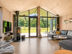 Ein modernes Wohnzimmer mit Kamin, einer Couch, einem Fernseher und einer großen Glasschiebetür, die zu einem Garten führt.