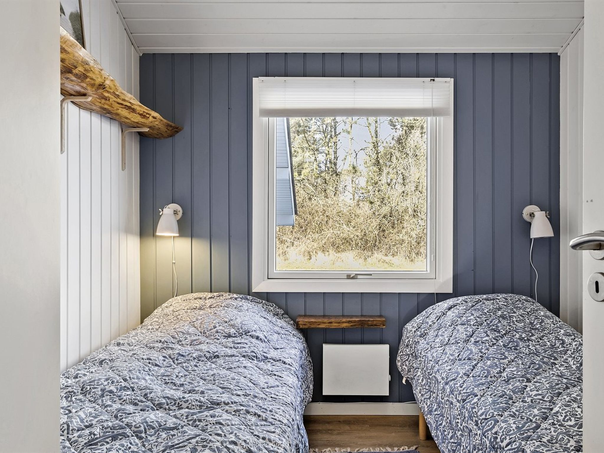 Ein Schlafzimmer mit zwei Betten, einem Fenster mit Blick auf Bäume und einer Holzablage.