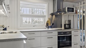 Una cocina moderna con gabinetes blancos, una campana extractora de acero inoxidable, un microondas integrado y una cafetera.