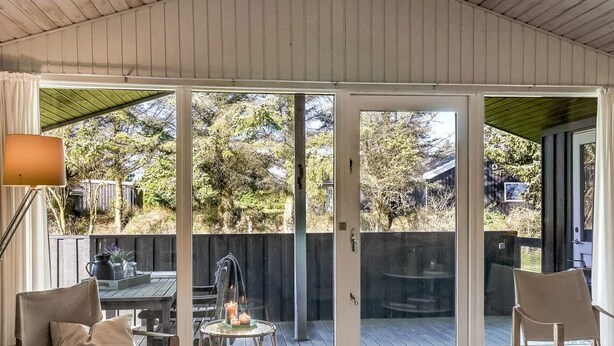 A covered patio with a wooden floor, a table with chairs, a small table with candles, and a view of a wooden fence and trees. - "Apsolon" - 600m from the sea by Interhome (Løkken)