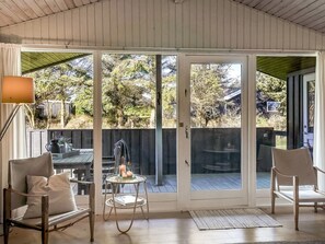 Une terrasse couverte avec un plancher en bois, une table avec des chaises, une petite table avec des bougies et une vue sur une clôture en bois et des arbres.