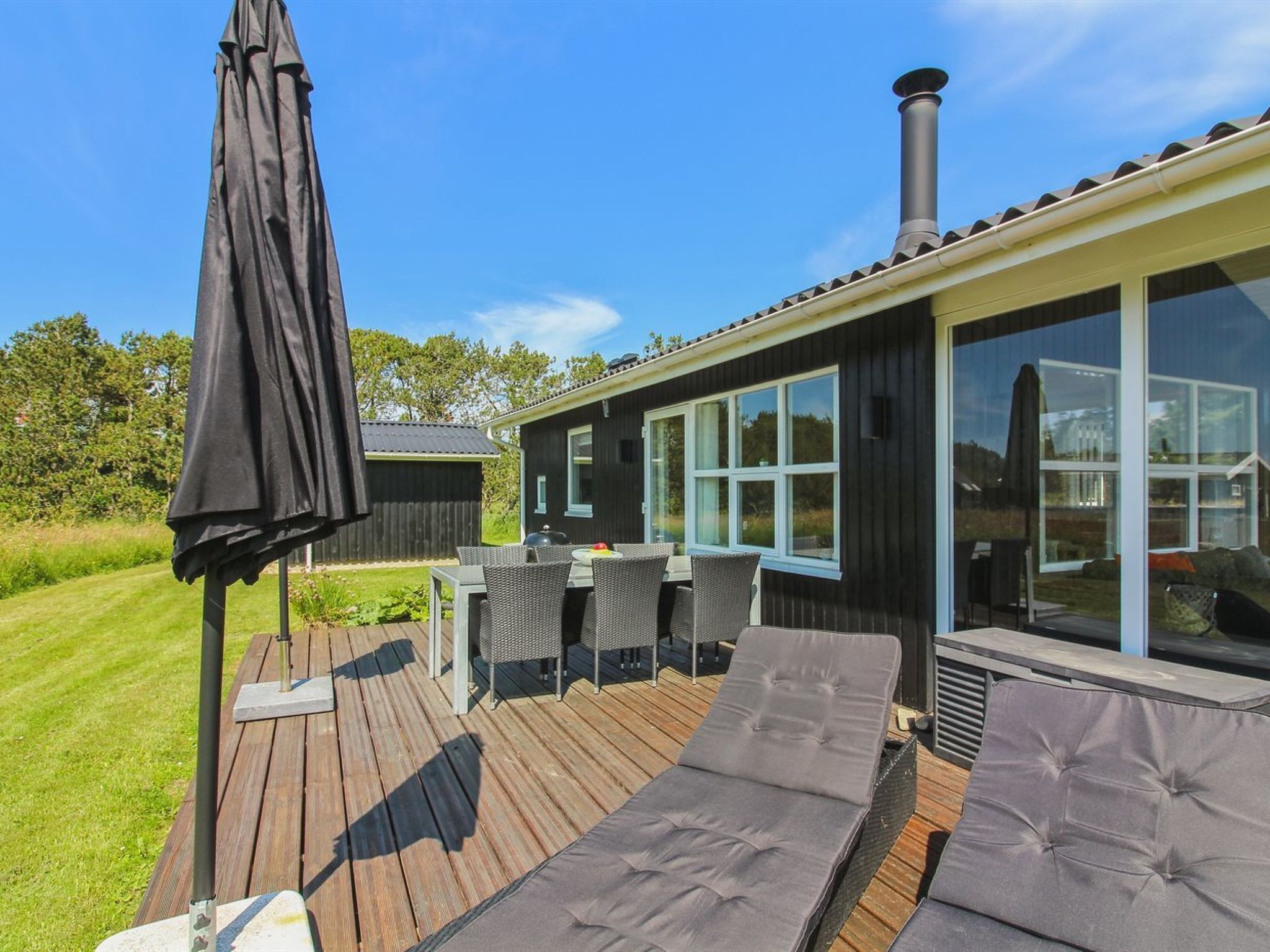 Een modern terras buiten, met een houten vloer, een barbecue en een groot raam met uitzicht op een gazon.