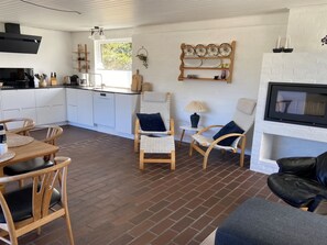 A modern kitchen with white cabinets, a dining table with chairs, a fireplace, and a TV mounted on the wall.