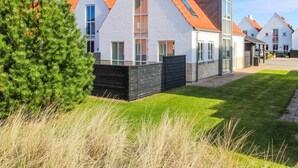 Een rij moderne huizen met schuine daken en grote ramen, omgeven door keurig onderhouden gazons en een hoge altijdgroene boom.