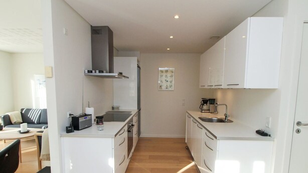Een moderne keuken met witte kasten, een centraal eiland en een zithoek met een bank en tafel.