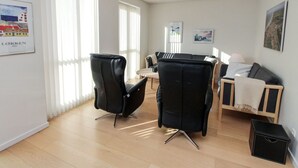 Een moderne woonkamer met een bank, twee zwarte stoelen, een bijzettafeltje en een lamp.