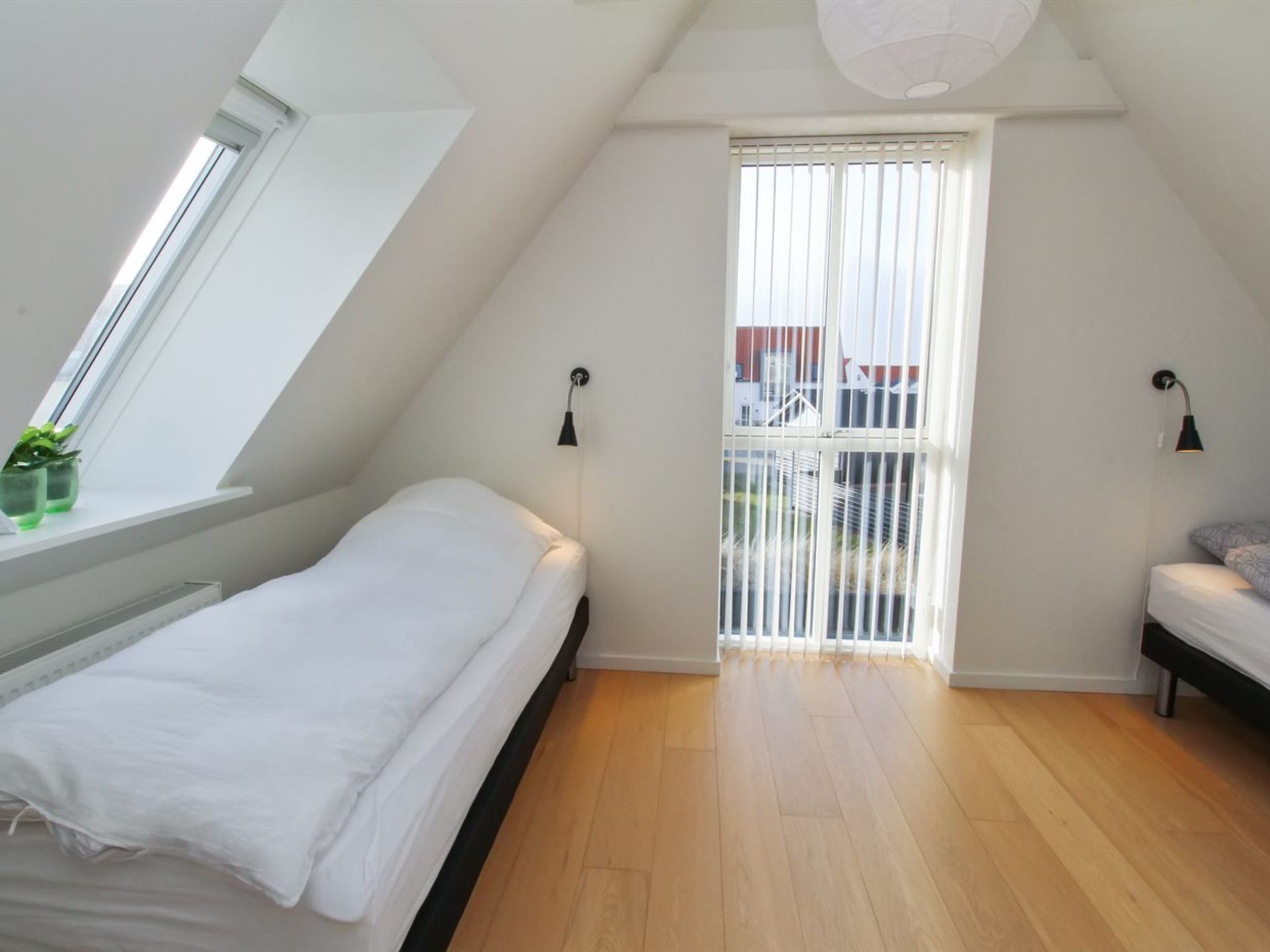 Una habitación peque ña y luminosa con techo inclinado, una cama individual, una ventana con persianas y una puerta que da al exterior.