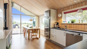 A modern kitchen with wooden cabinetry, a stainless steel refrigerator, and a dining area with a wooden table and chairs. - "Alma" - 500m from the sea by Interhome (Løkken)