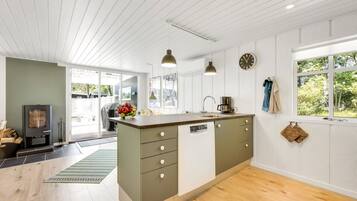 Une cuisine moderne dotée d’un îlot central, de planchers en bois et offrant une vue sur l’extérieur grâce à de grandes fenêtres.