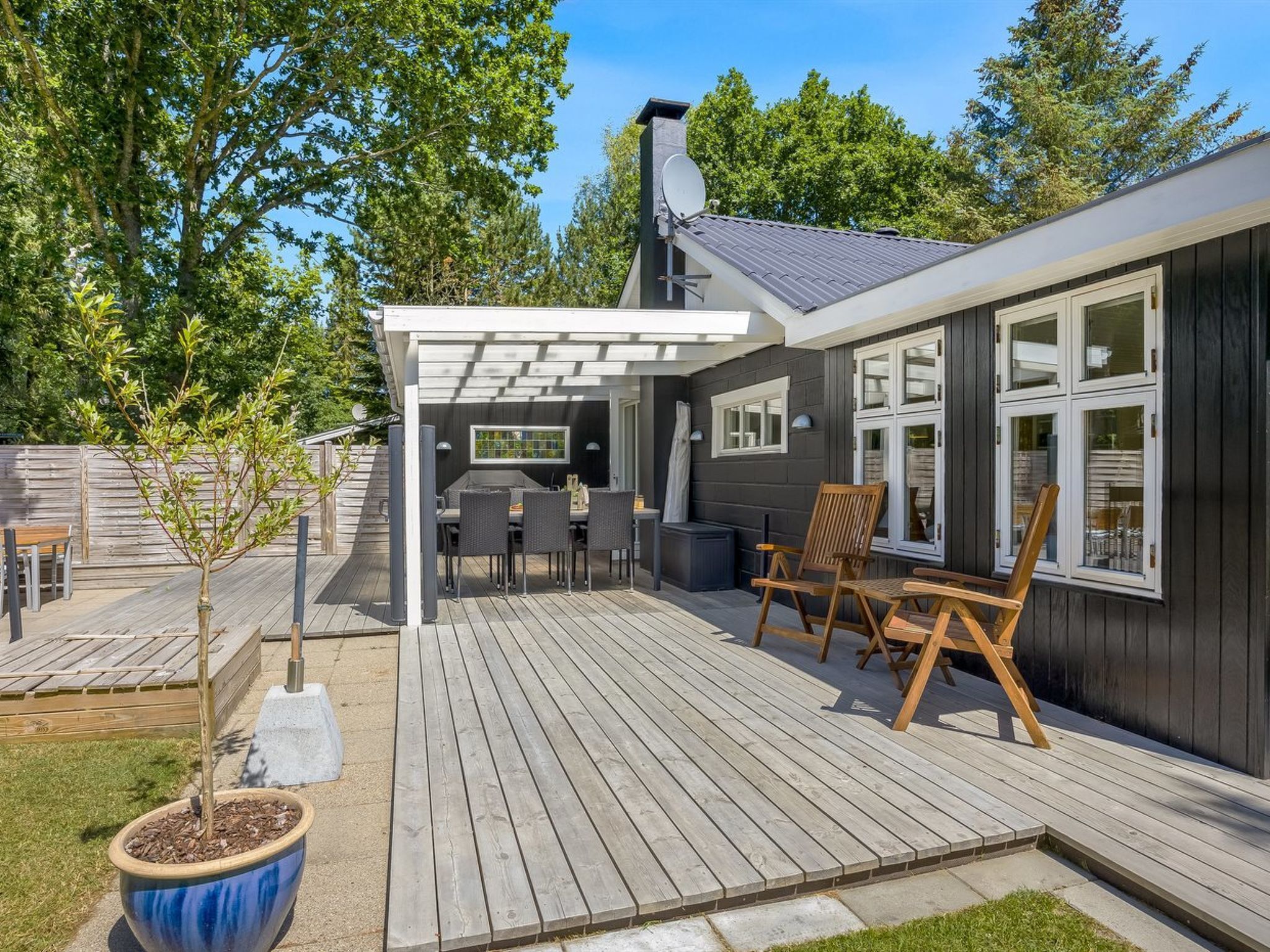 Une terrasse en bois avec des meubles d’extérieur, une pergola et une vue sur la maison.