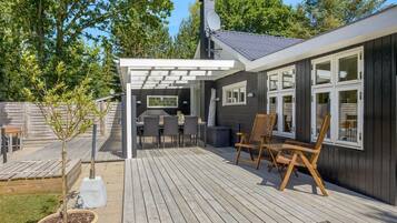 Une terrasse en bois avec des meubles d’extérieur, une pergola et une vue sur la maison.