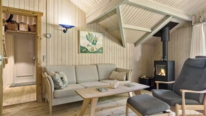 Een gezellige kamer met een houten plafond, een bank, een tafel, een stoel en een houtkachel.