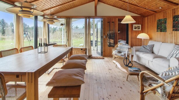 A spacious room with a wooden ceiling, a dining table with benches, a sofa, and a large window offering a view of the outdoors. - "Nestori" - 950m from the sea by Interhome (Løkken)