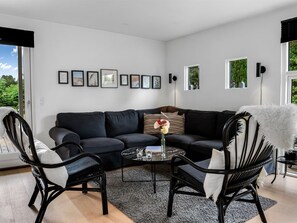 A modern living room with a black sofa, two black chairs, a coffee table, and framed pictures on the wall.