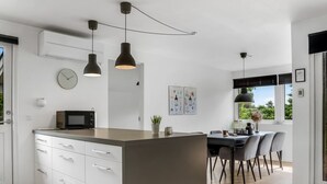 Een moderne keuken met een centraal eiland, witte kasten en hanglampen.
