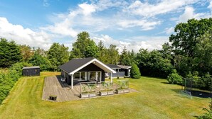 Ein modernes Haus mit Terrasse, einer kleinen Gartenhütte und einem gepflegten Rasen.