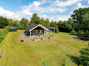 Une maison moderne dotée d’une terrasse, d’un petit abri de jardin et d’une pelouse bien entretenue.