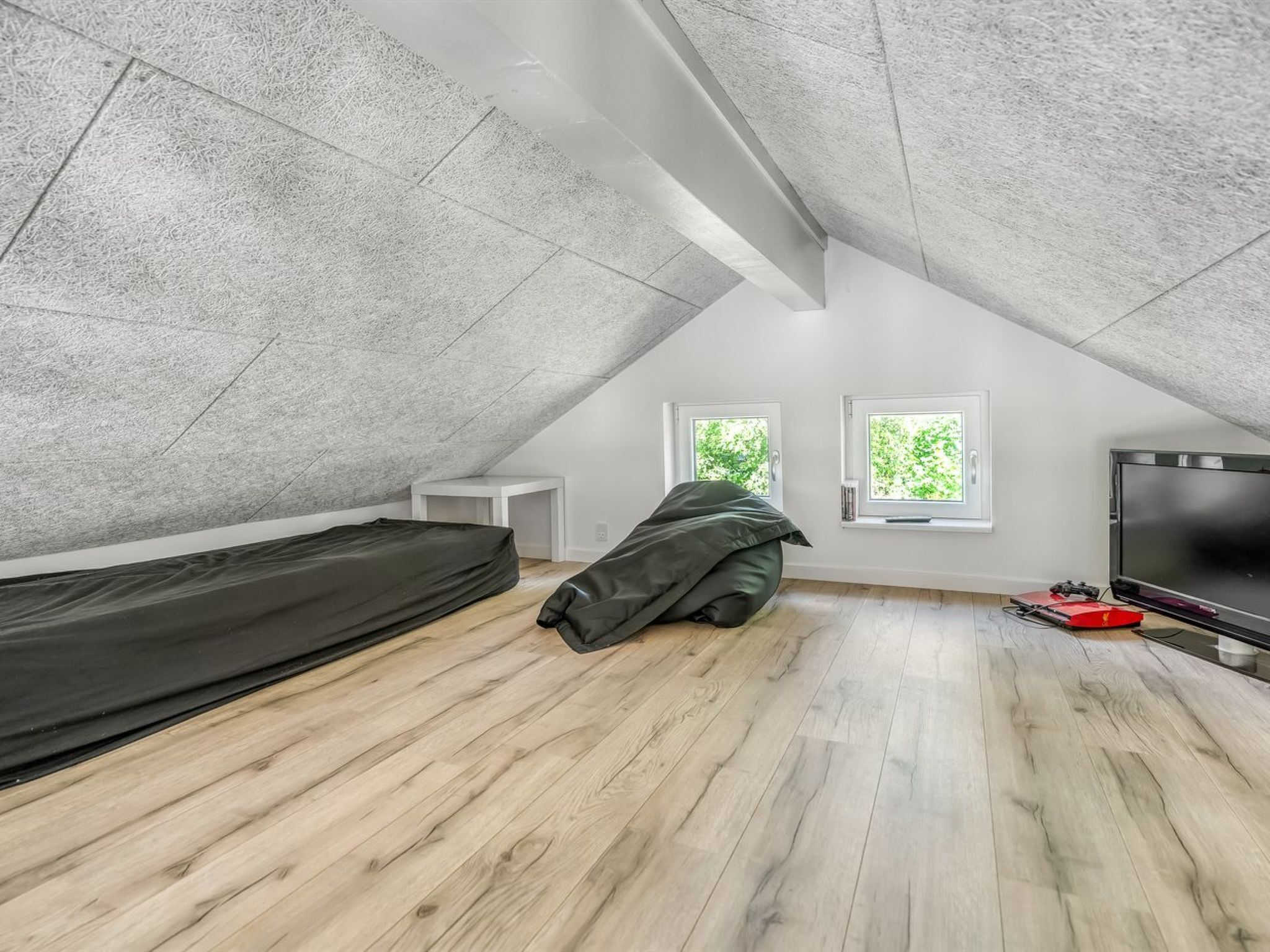 Ein kleines, modernes Schlafzimmer im Dachgeschoss mit schrägen Wänden, einem Bett, einem Fernseher und zwei Fenstern.