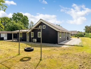 A modern house with a dark exterior, a covered porch, and a swing set.
