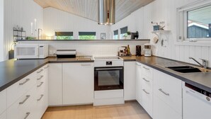 Une cuisine moderne avec des meubles blancs, une hotte en acier inoxydable, un four encastré et un plan de travail noir.