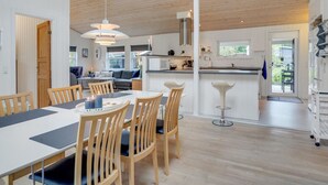 Une cuisine moderne dotée d’un îlot central, d’un coin repas avec une grande table et des chaises, et offrant une vue sur l’extérieur grâce à une porte vitrée.