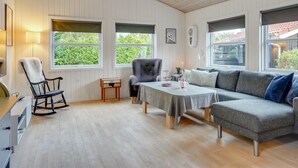 Une pièce spacieuse avec un plafond en bois, un canapé gris, une table à manger et un fauteuil à bascule.