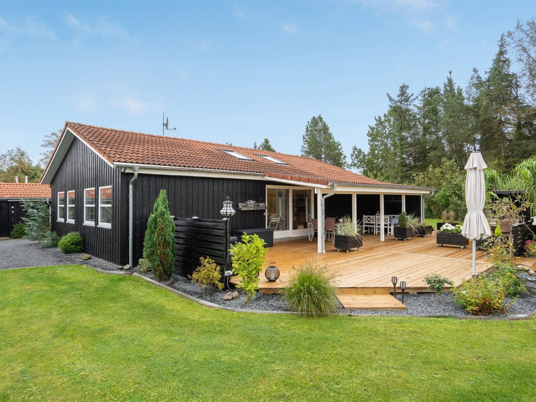 A modern house with a wooden deck, a covered patio, and a well-maintained garden.