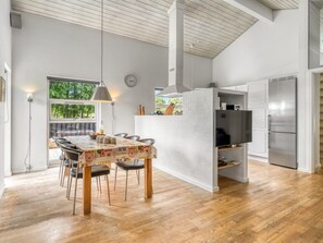 A modern kitchen with a built-in oven, a dining area with a table and chairs, and a large window overlooking greenery.