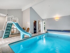 An indoor swimming pool with a blue slide, a small table with chairs, and a door leading to a bathroom.