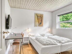 A bedroom with a bed, a desk, a chair, a television, and a window with a view of greenery.