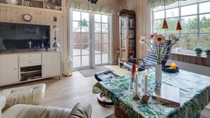 Un salon chaleureux avec une télévision, un coin salon et une table à manger recouverte d’une nappe aux motifs tropicaux.